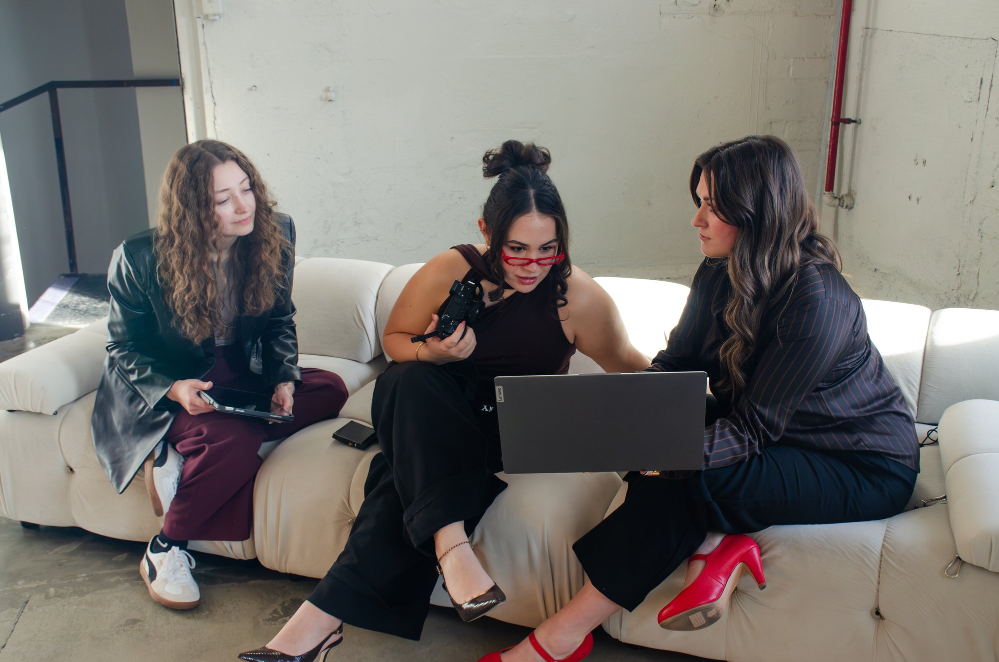 Sophia Pearle sitting between two clients on a studio sofa, camera in hand, reviewing content together on a laptop.