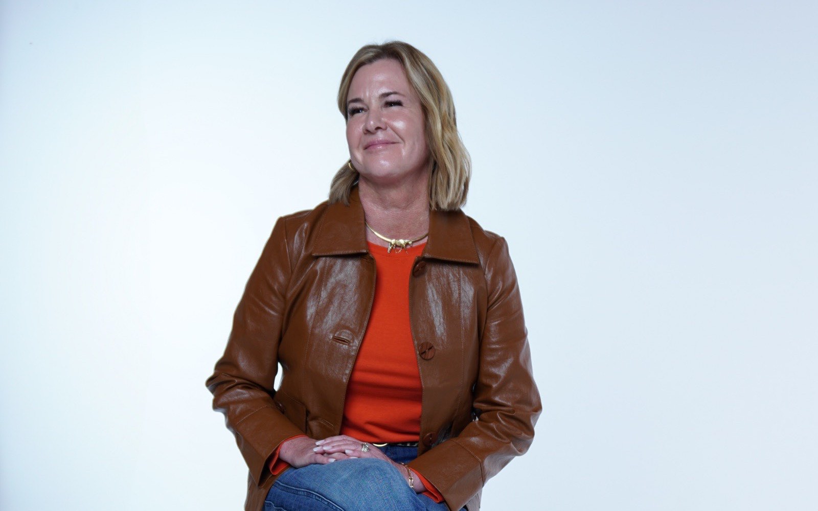 Keely Matteo, a mortgage loan officer in a tan leather jacket, seated on a stool in a bright studio.